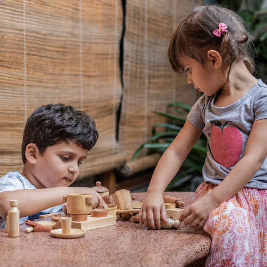 Two children playing together with a wooden pretend play kitchen set, a meaningful Rakhi gift idea for kids from The Toy Trunk.