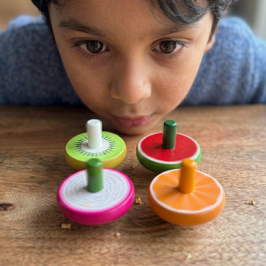 Child watching wooden fruit-shaped spinning tops spin on a wooden surface, screen-free traditional play for kids 3 to 5 years in India