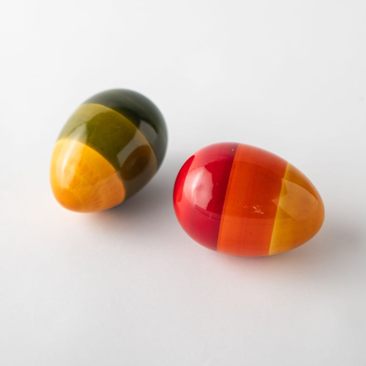 Two glossy wooden egg rattles with vibrant, multi-colored striped patterns in red, yellow, and green, displayed on a clean white background.