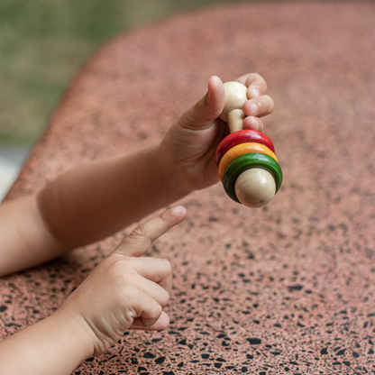 Baby holding wooden dumbbell rattle for early grasping and sound play.