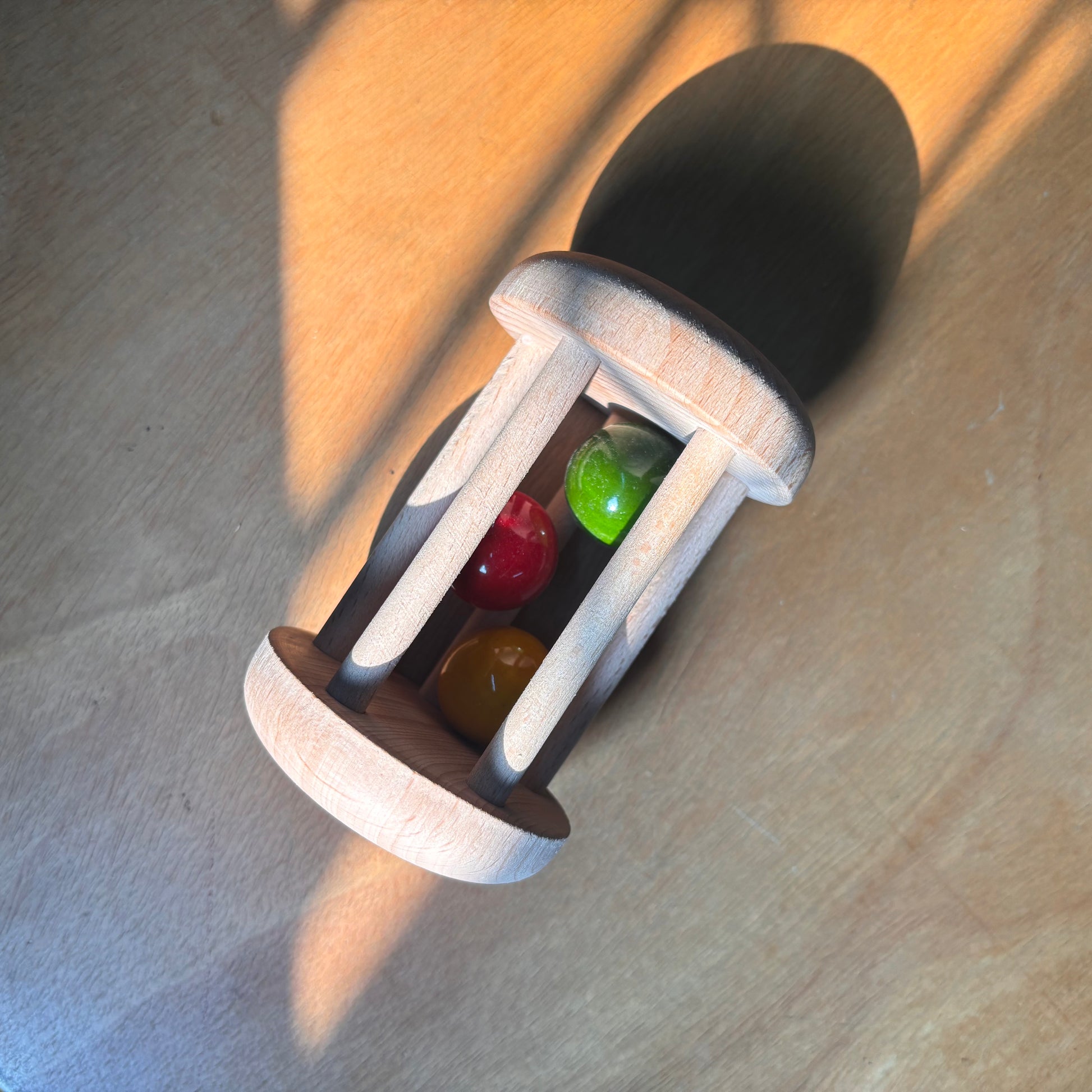 Top-down view of an eco-friendly wooden rattle with red, yellow, and green balls, captured in natural sunlight.