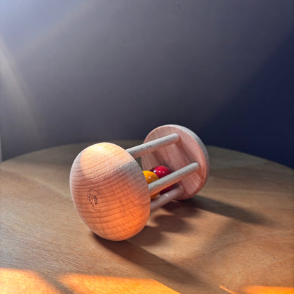Close-up shot of a smooth, natural wood rolling rattle for babies, showing the grain of the wood and the maker's stamp.