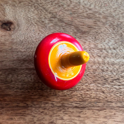 Red and yellow wooden finger spinning top, handcrafted traditional toy for kids.