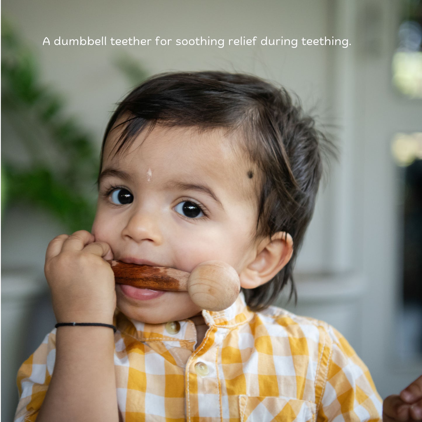 The Toy Trunk toddler holding and chewing on wooden dumbbell teether for safe teething relief