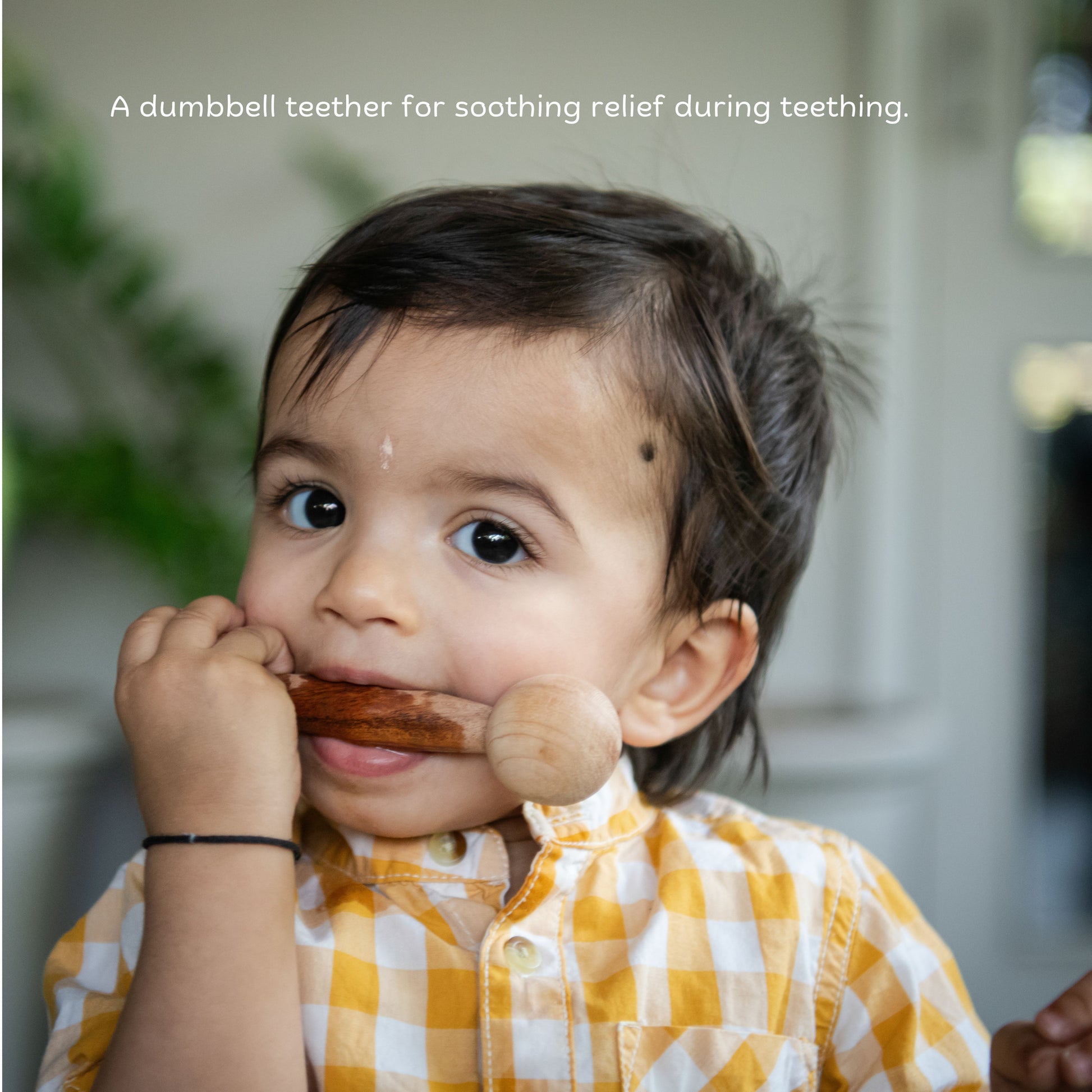 The Toy Trunk toddler holding and chewing on wooden dumbbell teether for safe teething relief