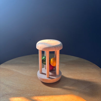 Wooden rolling rattle standing upright with colourful balls for toddler sound play.