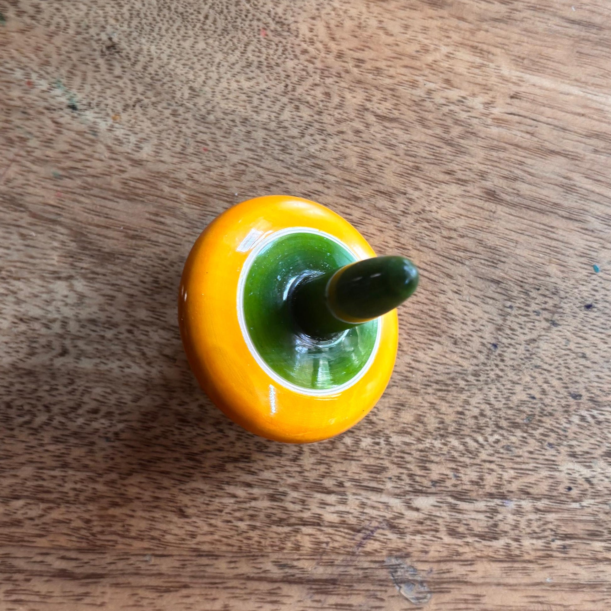 Yellow and green handmade wooden finger spinning top for fine motor skill play.